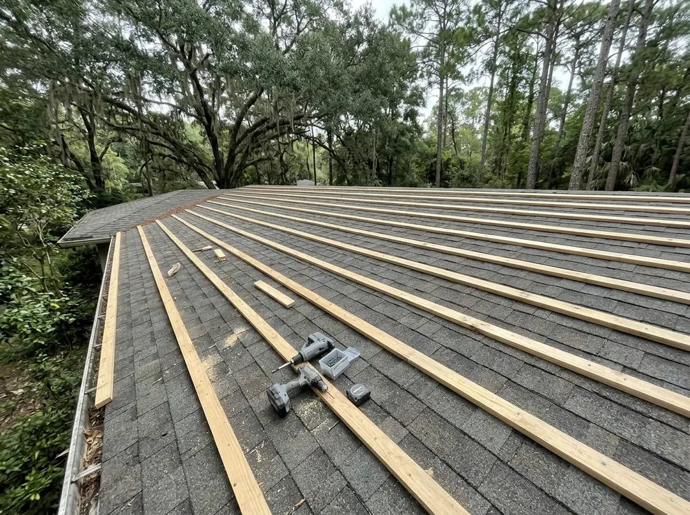 Rows of wood furring strips screwed over old asphalt shingles on a ranch house roof