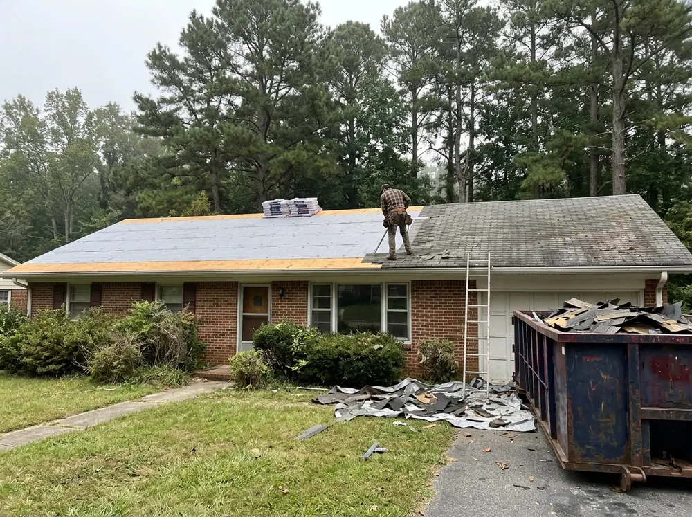 Roof deck half stripped of old asphalt shingles with fresh synthetic underlayment ready for metal panels
